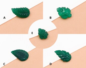 Puede incluir: Cinco cabujones de forma de hoja tallados en verde, cada uno con un diseño único, se muestran sobre una superficie rosa claro. Los cabujones están dispuestos en círculo, con las letras A, B, C, D y E etiquetando cada uno de ellos.