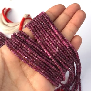 May include: A strand of small, faceted, deep magenta-coloured cube-shaped beads. The beads are strung together in a long, continuous line, showcasing a uniform square cut and a rich, saturated pinkish-purple hue throughout the entire length.