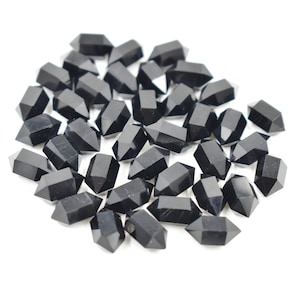 May include: A collection of small, black, double-terminated crystal points. Each crystal has a faceted, geometric shape and a polished, reflective surface. The crystals are scattered on a white background.