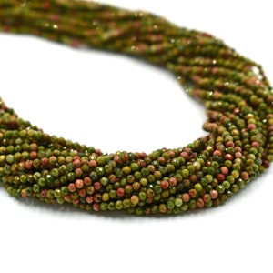 May include: A strand of green and red gemstone beads. The beads are small and round, and they have a faceted finish. The beads are strung on a clear thread.