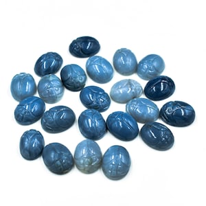 Può includere: Una collezione di 20 cabochon blu a forma di scarabeo. I cabochon sono di forma ovale e hanno una finitura liscia e lucida. Variano di colore dal blu chiaro al blu scuro.