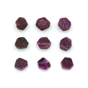 May include: Nine small, faceted, ruby red gemstones. The gemstones are hexagonal in shape and have a rough, natural finish.