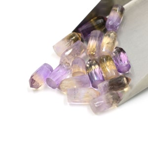 May include: A collection of faceted amethyst, citrine, and amethyst-citrine gemstone points in a variety of shades of purple, yellow, and brown.