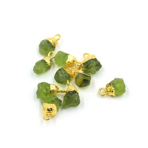 May include: A group of ten green gemstone pendants with gold-plated jump rings. The gemstones are rough and have a natural, unpolished look.