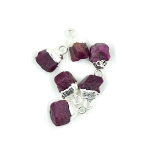 May include: Six small, raw ruby gemstone pendants with silver-plated caps and jump rings. The rubies are a deep red color and have a rough, natural texture.