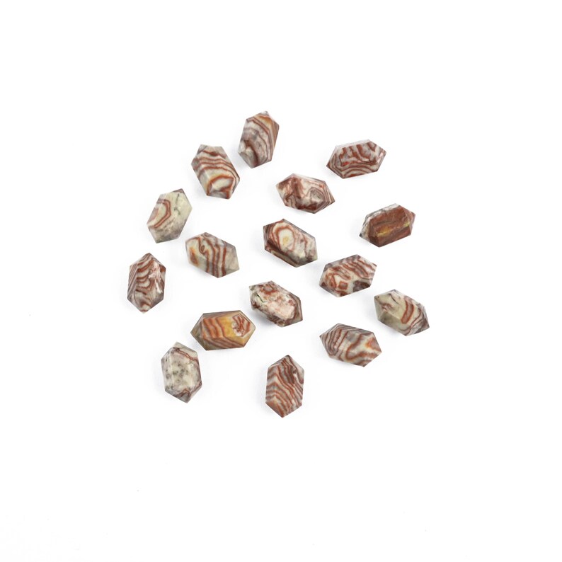 May include: A scattering of small, hexagonal stones, each displaying a mix of tan, brown, and white striped patterns. The stones are arranged on a white backdrop, highlighting their natural colours and textures. These stones could be used for jewellery or decorative purposes.