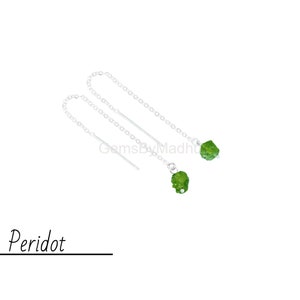 May include: A pair of silver dangle earrings with green peridot gemstones. The earrings have a delicate chain design and are perfect for adding a touch of elegance to any outfit.