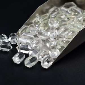 May include: A metal scoop filled with clear quartz crystals. The crystals are faceted and have a variety of shapes and sizes.