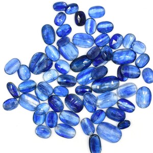 May include: A collection of oval-shaped blue kyanite gemstones. The stones have a striated pattern and range in size and shade of blue.
