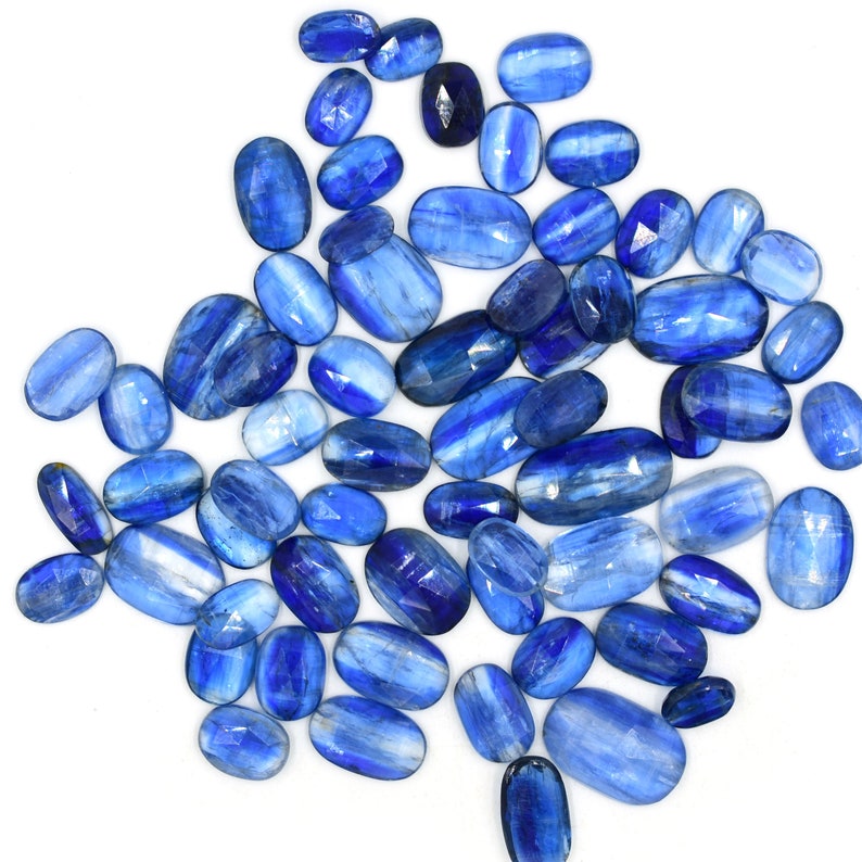 May include: A collection of oval-shaped blue kyanite gemstones. The stones have a striated pattern and range in size and shade of blue.