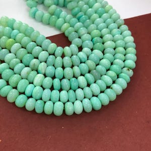Puede incluir: Un collar de cuentas ovaladas de color verde claro. Las cuentas tienen una superficie lisa y pulida y están ensartadas, creando un collar o una pulsera. Las cuentas son una mezcla de tonos verdes claros y medios.