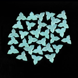May include: A collection of light blue, faceted, four-pointed star-shaped chalcedony gemstone beads. The beads are scattered on a black background.