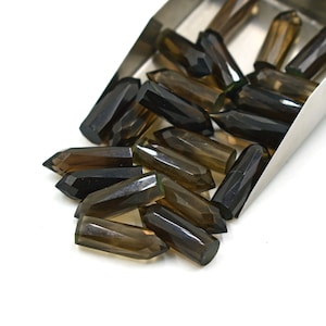 May include: A pile of smoky quartz crystal points in a metal scoop. The points are faceted and have a dark brown colour.