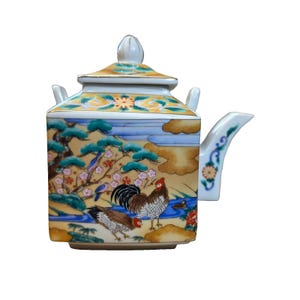 May include: A square ceramic teapot with a lid, featuring a colorful hand-painted scene of two roosters, pine trees, and flowering branches against a yellow background. The spout and lid handle are white with small floral accents and gold trim.