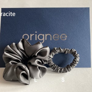May include: A large and a small anthracite-colored satin hair scrunchie set. The items are displayed in front of a dark blue card featuring the text "orignee" in gold lettering, with the word "anthracite" printed in white in the top left corner.