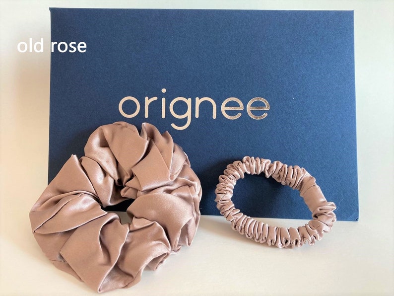 May include: Two old rose colored hair accessories, one large scrunchie and one thin hair tie, positioned in front of a dark blue rectangular card with the text originee printed in gold and the words old rose printed in white.