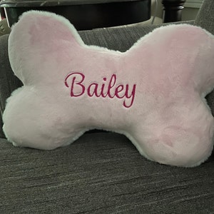 May include: Pink plush dog bone shaped pillow with the name Bailey embroidered in pink.