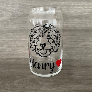 May include: A clear glass can with a black and white image of a dog's face and the name "Henry" with a red heart.