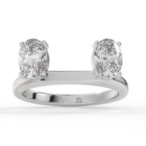 Puede incluir: Un anillo de plata con dos gemas ovales. Las gemas están colocadas a ambos lados de una barra horizontal, creando un diseño moderno. El anillo está sobre un fondo blanco.