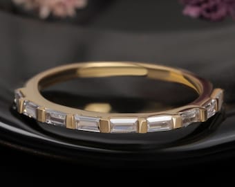 May include: A gold band ring with a row of small, rectangular-shaped clear stones.