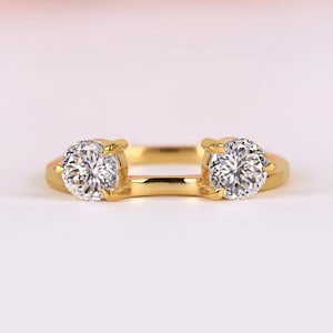 May include: A gold ring with two round, clear gemstones. The ring has a simple, elegant design, with the gemstones set on either side of the band. The ring is likely a jewelry item, such as an engagement ring or a wedding band.