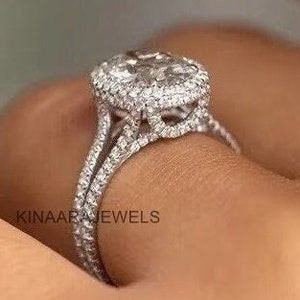 May include: A close-up of a diamond ring with a halo setting. The ring features a large, oval-cut diamond surrounded by smaller diamonds. The band is split and also encrusted with diamonds. The text "KINAARA JEWELS" is visible.