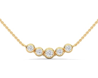 Può includere: Una delicata collana d'oro con cinque pietre preziose rotonde e trasparenti incastonate in castoni individuali. Le pietre sono disposte in una curva delicata, sospese a una sottile catena d'oro. La collana è su sfondo bianco.