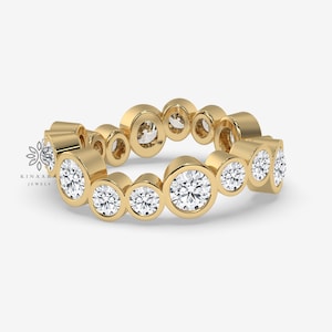 May include: A gold band ring featuring a row of bezel-set round diamonds. The diamonds are of varying sizes, creating a graduated effect.