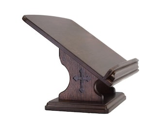 May include: A dark brown wooden lectern with a cross carved into the front. The lectern has a slanted top surface and a base with a decorative design.