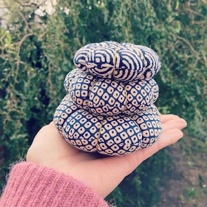 May include: A stack of three round fabric pincushions. The pincushions are covered in a blue and white geometric pattern. The top pincushion has a wavy pattern.