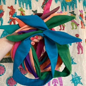 Puede incluir: Un conjunto de diademas de tela de colores en tonos turquesa, verde, naranja, rosa y morado. Las diademas están atadas en un nudo y están listas para ser usadas.