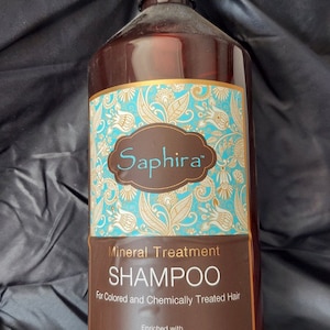 May include: A brown plastic bottle of Saphira Mineral Treatment Shampoo for colored and chemically treated hair. The bottle is labeled with 26 Dead Sea Minerals, pure keratin, sulfate/paraben free, color saver, and 34 oz.