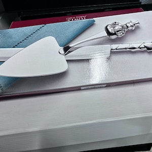 May include: A silver serving set with a snowman and candy cane design. The set includes a cake server and a knife. The packaging features the Towle Holiday Wishes logo and the words "Dessert Server".