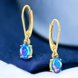 May include: A pair of gold dangle earrings with a blue opal gemstone. The earrings have a lever back closure.
