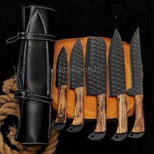 May include: A set of six black kitchen knives with wooden handles, displayed on a wooden cutting board. The knives have textured blades and are accompanied by a black leather knife roll. The text "SharpSpotUS" is visible on the image.