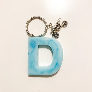 May include: A light blue resin letter D keyring with a silver dirt bike charm attached to a silver key ring.