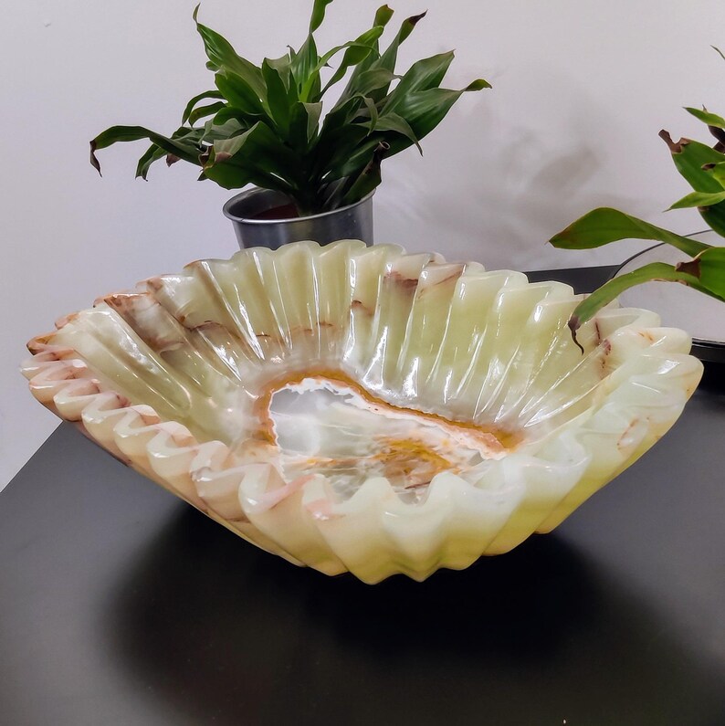 Puede incluir: Un cuenco decorativo, de forma cuadrada con borde ondulado. El cuenco est&aacute; hecho de una piedra transl&uacute;cida de color verde claro con vetas marrones y blancas. El interior tiene un centro m&aacute;s claro, casi blanco.