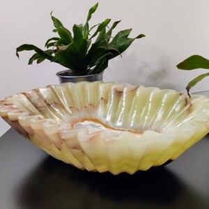 Puede incluir: Un cuenco decorativo grande hecho de &oacute;nix transl&uacute;cido. El cuenco tiene un borde ondulado y una combinaci&oacute;n de colores verde claro y marr&oacute;n. El interior tiene un patr&oacute;n blanco y naranja. El cuenco est&aacute; sobre una superficie negra.