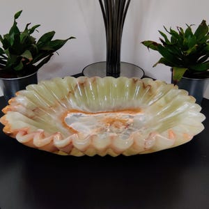 Puede incluir: Un cuenco decorativo ovalado de &oacute;nix con borde festoneado. Presenta una combinaci&oacute;n de colores verde claro y naranja, con un interior veteado. Este objeto decorativo es ideal para exhibir. Dimensiones: aproximadamente 30 cm de largo.