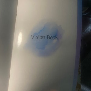 May include: A white book with a blue watercolour design and the text "Vision Book" on the cover.
