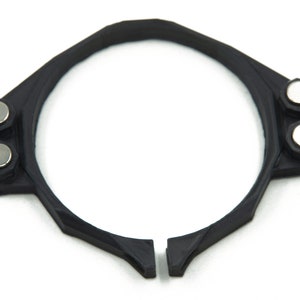 May include: A black plastic ring with two silver magnets on the side. The ring is designed to hold a watch face.