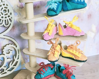 Op de afbeelding: Een houten plank met zes vilten schoenen in verschillende kleuren, waaronder blauw, groen, geel, roze en rood. De schoenen zijn in paren op de planken gerangschikt.