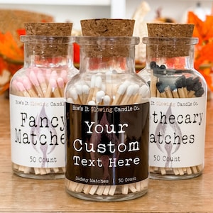 May include: Three glass jars filled with matches, each with a different label. The labels are black with white text. The first jar says "Fancy Matches" and has pink matches. The second jar says "Your Custom Text Here" and has white matches. The third jar says "Apothecary Matches" and has black matches.