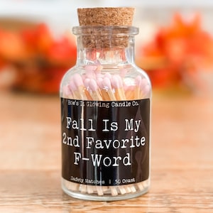 May include: A glass jar filled with 50 pink-tipped matches. The jar has a black label that reads "How's It Glowing Candle Co." and "Fall Is My 2nd Favorite F-Word".