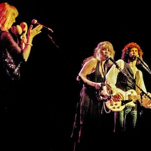 Puede incluir: Tres músicos actuando en un escenario. Una mujer con cabello rubio canta en un micrófono mientras sostiene un pandero. Otra mujer con cabello largo castaño toca la guitarra. Un hombre con cabello largo castaño toca la guitarra y canta en un micrófono.