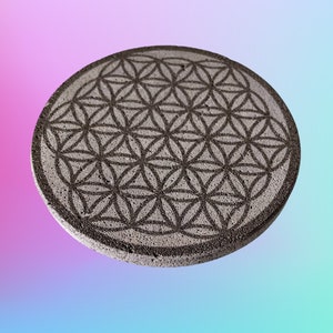 Peut inclure: Un dessous de verre rond en pierre grise avec un motif géométrique noir en forme de fleur de vie.