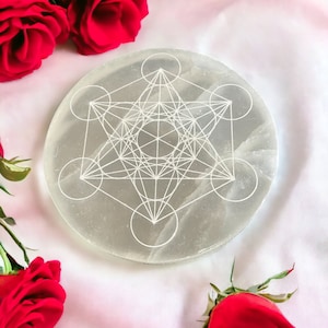 Könnte beinhalten: Eine weiße Selenit-Ladestation mit einem weißen geometrischen Design, umgeben von roten Rosen auf weißem Hintergrund.