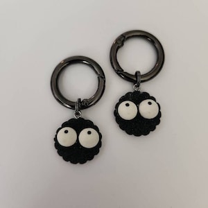 May include: Two black metal keychains with black and white cartoon characters attached. The characters have large white eyes and a black, fuzzy body.