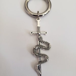 May include: A silver key chain with a sword and snake design. The sword is straight and the snake is coiled around it.