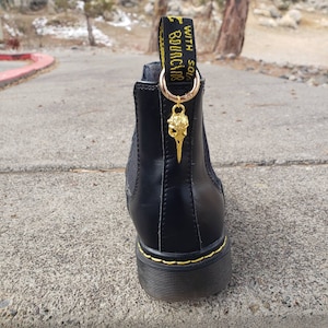 May include: Black leather ankle boots with a yellow and black tag that reads "with soles bouncing". A gold skull charm hangs from the tag.